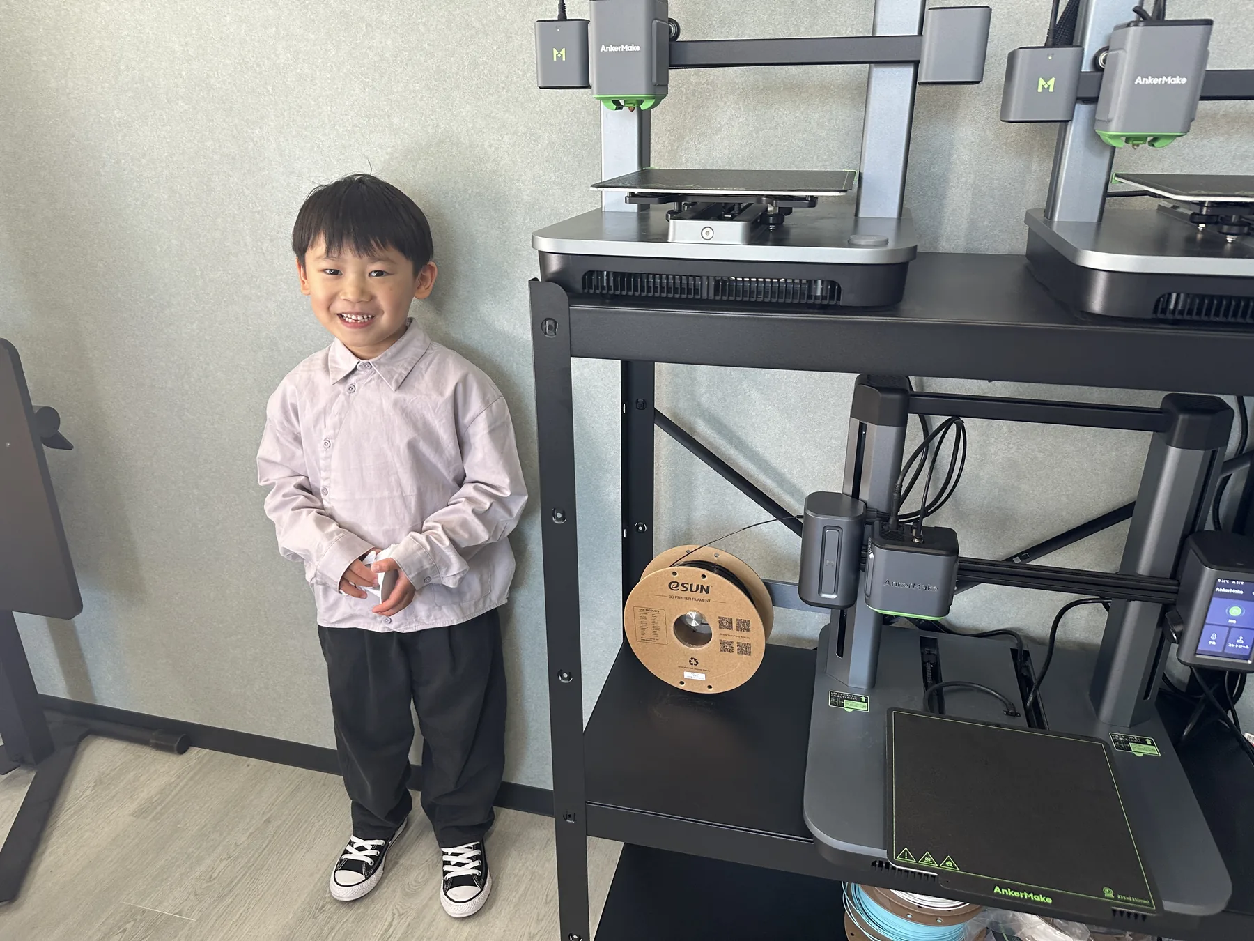 3Dプリンタの前で作品を見せる子ども